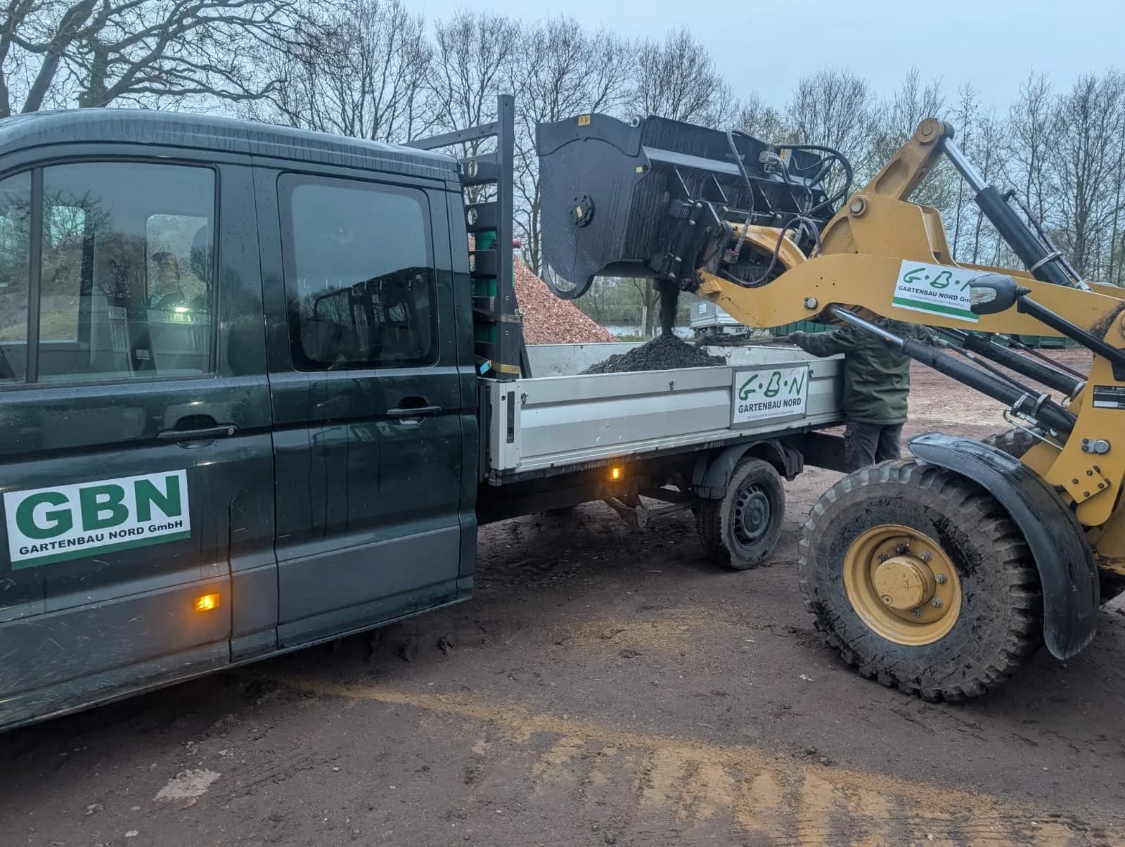 GBN-Radlader belädt einen grünen GBN-Pritschenwagen mit Mutterboden auf dem Betriebshof im Kreis Pinneberg